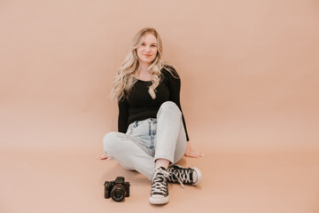 Young female photographer sitting with a camera on a beige background