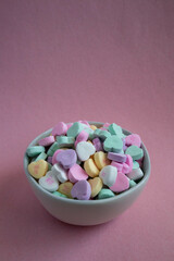 Conversation colorful candy hearts in white bowl on pink background