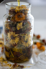 Close up of oil being poured into glass jar filled with dried flowers