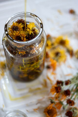 Top view of oil being poured into glass jar filled with dried flowers