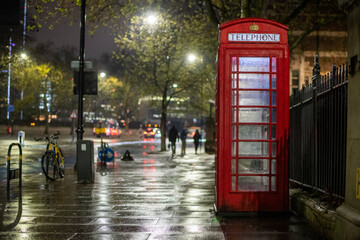 Naklejka premium Iconic red phone booth at night on a wet rainy London street