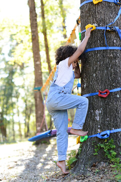 Child climbing a tree with colorful grips, barefoot, focused in