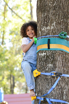 A smiling child in overalls climbs a tree with colorful foothold