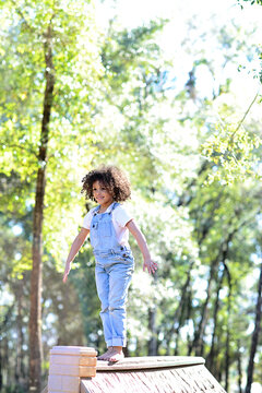 A child in overalls balances barefoot on a playhouse roof in the