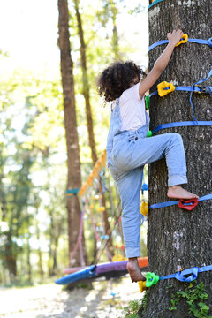 Child climbing a tree using colorful grips, barefoot, in a playf