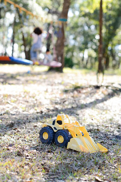 Yellow toy bulldozer on grassy ground with children playing in t