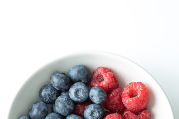 Top down closeup view of fresh blueberries and raspberries in the white bowl with space for text