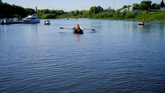 Water and boat recreation. People are rowing in life jackets in good weather. Catamarans are floating nearby and small yachts are moored.