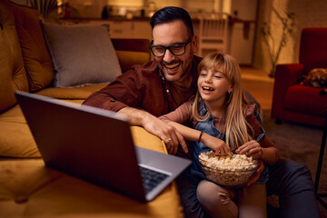Happy father and daughter watching movie on laptop at home.