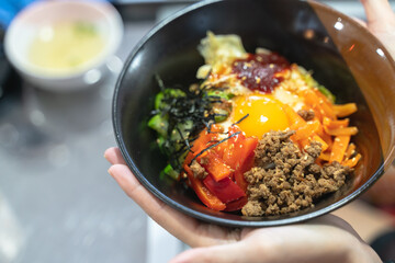 Close-up of a vibrant Korean bibimbap bowl with fresh ingredients like egg yolk, vegetables, and minced meat.