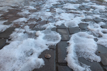 Gray paving slabs on a pedestrian bridge. There are white islands of unmelted snow on the surface....