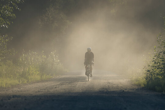 Solo biker on a dirt trail in a forest, with blowing dust