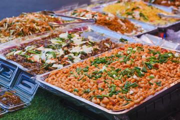The dishes include different types of noodles, pasta, and stir-fried vegetables. The food is arranged in an organized manner, with each tray containing a different dish.