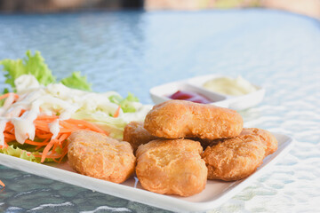 plate of food placed on a glass table.The plate contains several golden-brown fried chicken nuggets,alongside a side of fresh salad consisting of lettuce,and cabbage drizzled with a white dressing.