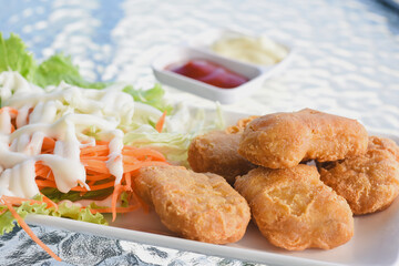 plate of food placed on a glass table.The plate contains several golden-brown fried chicken nuggets,alongside a side of fresh salad consisting of lettuce,and cabbage drizzled with a white dressing.