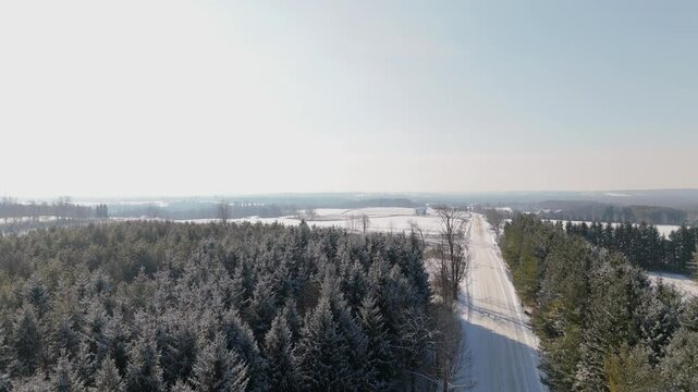 Crane drone shot of snowy sideroad and forest in Caledon, Ontario, Canada