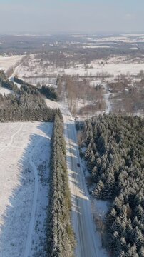 Vertical flyover drone shot of snowy sideroad and forest in Caledon, Ontario, Canada