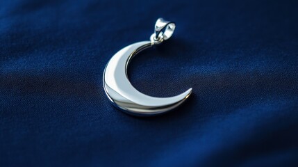 Silver crescent moon pendant resting on dark blue fabric in natural light