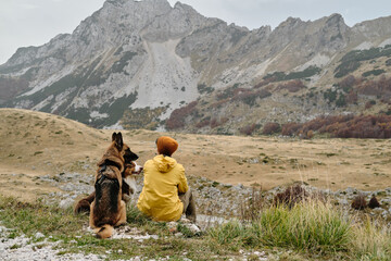 Fototapeta premium Breathtaking mountain landscape with traveling young woman and her dogs. Rear view. Travel with pet concept. Montenegro, Durmitor National Park. Saddle Pass. Alpine meadows in autumn season.