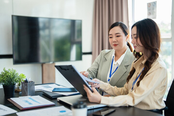 Confident mature business professional woman talking to younger female colleague at office table,...