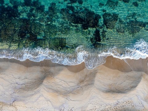 Aerial view of a pristine beach with turquoise waters and gentle waves crashing on the sandy shore