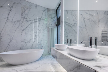 Modern bathroom design decorated with marble tiles. A bathtub by the window, stylish accessories...