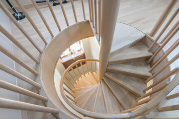 Spiral staircase made of natural light wood, in a country house. View from above.
