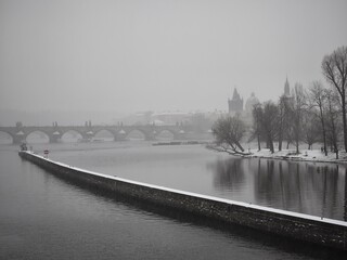 with charles bridge spanning the vltava river, surrounded by snow covered trees and historic...