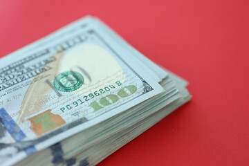 Big amount of hundred dollar bills in thick stack lies on bright red color paper background