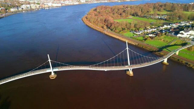 Wide aerial of The Peace Bridge and River Foyle in Derry-Londonderry on a bright sunny day. The camera moves right to left. Filmed in 4K, 60fps and with Rec709 color.