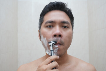 A man shaves his beard with foam and razor. Personal care and skin care concept.