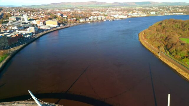 Wide reversing aerial travelling over the River Foyle and Peace Bridge in Derry-Londonderry. The camera reverses to reveal the bridge and surrounding area. Filmed in 4K, 60fps and in Rec709 color.