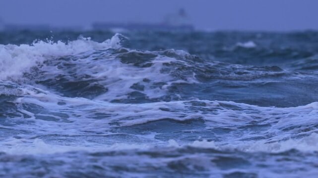 Close-up of rough ocean waves with a distant cargo ship visible
