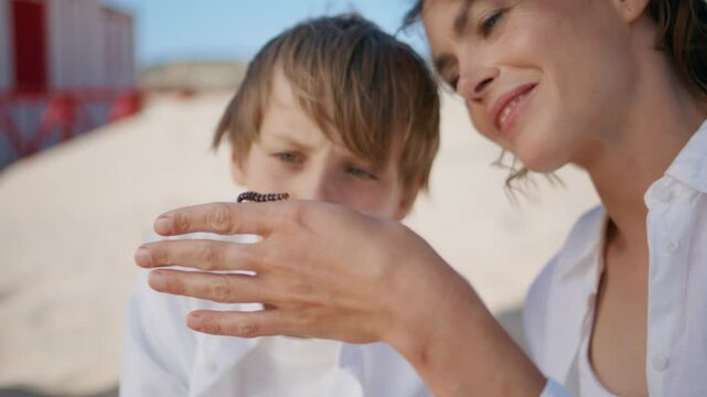 Curious mother boy observing caterpillar on sandy beach closeup. Smiling mom son