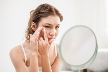 Young beautiful Asian woman checking her facial skin in mirror feeling worried about freckles...