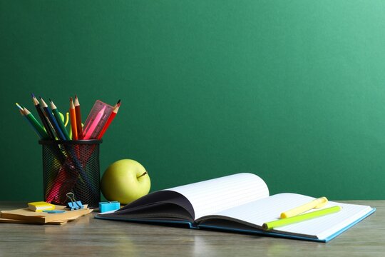Back to school. Close-up of colorful stationery, textbooks, green apple on green chalkboard
