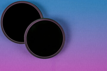 Two black camera lens filters on a gradient blue to purple background