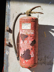 Rusted Fire Extinguisher Against a Weathered Concrete Wall in Sunlight