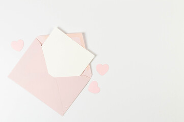 Top view of pink envelope, white card on white background. Valentine's day, pink hearts, love. Post flat lay, copy space.