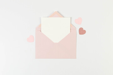 Top view of pink envelope, white card on white background. Valentine's day, pink hearts, pink glitter heart, love. Post flat lay, copy space.