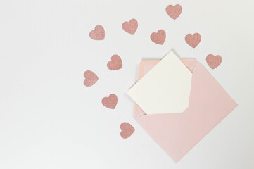 Top view of pink envelope, white card on white background. Valentine's day, pink glitter hearts, love. Post flat lay, copy space.