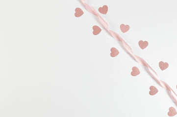 Top view of pink ribbon and pink glitter hearts on white background. Valentine's day, love. Shiny rolled fabric, silk and satin material. Copy space, flat lay.