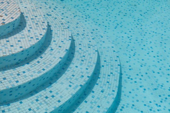background with clear blue swimming pool water with mosaic tiles and stair steps in summer