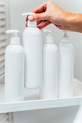 Cosmetician's hand takes the white cosmetic bottle dispenser from the shelf. Beauty and modern cosmetics treatments and products concept.