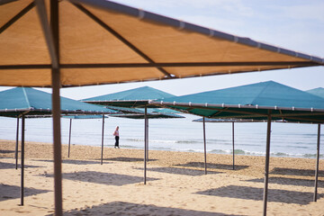 Beachfront Area with Empty Umbrellas and Lone Visitor by the Seashore