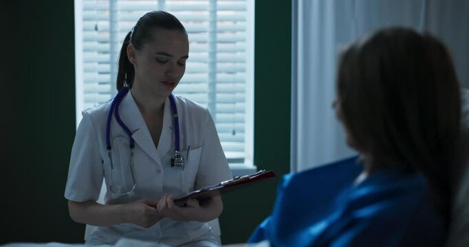 Doctor beside elderly patient in hospital room, presenting paperwork for her to sign.