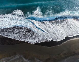 aerial view of ocean waves hitting the black sand beach with white foam
