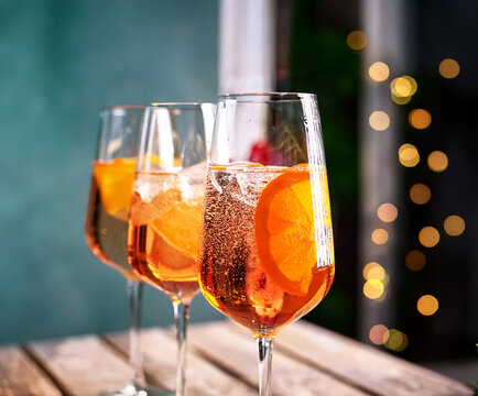 Photo of cocktail "Aperol Spritz" on a dark background: a transparent glass with orange drink, ice and a slice of orange. Bright and refreshing, perfect for good company.