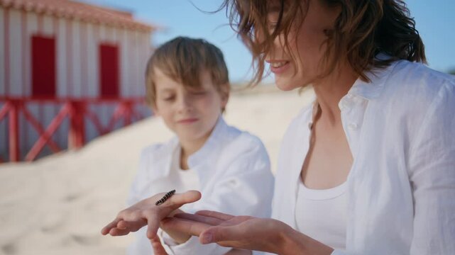Smiling mother child exploring caterpillar on beach sand closeup. Joyful mom son