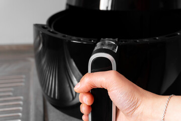 Closeup of female hand opening the basket of a black XXL air fryer. Homemade healthy fast tasty...